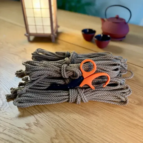 Bundles of jute rope with orange EMT shears on a wooden table, a paper lamp and a teapot behind